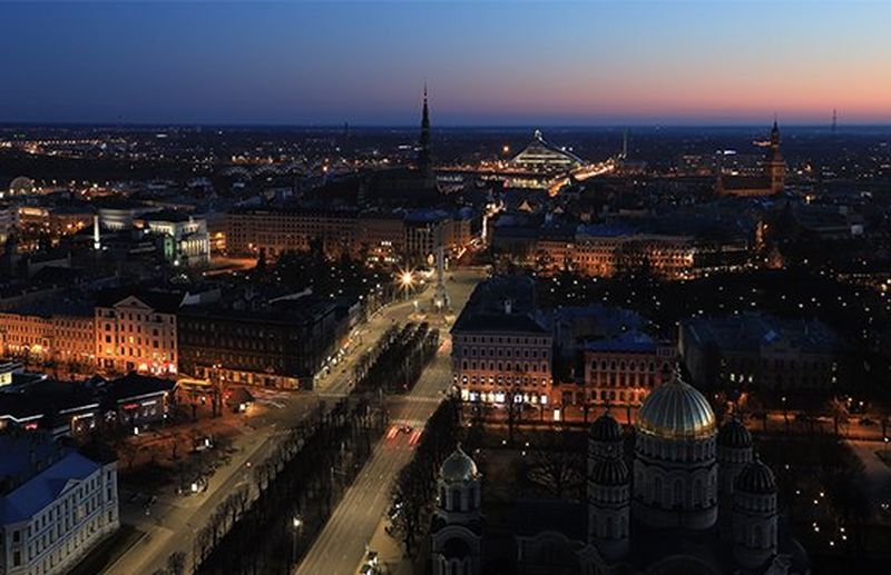 An aerial view of a city at night, many buildings illuminated below a dark blue sky streaked with pink.