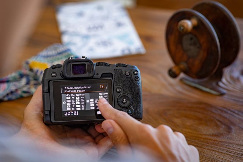 Человек касается опции на заднем экране камеры Canon, где отображается экран назначения кнопок.