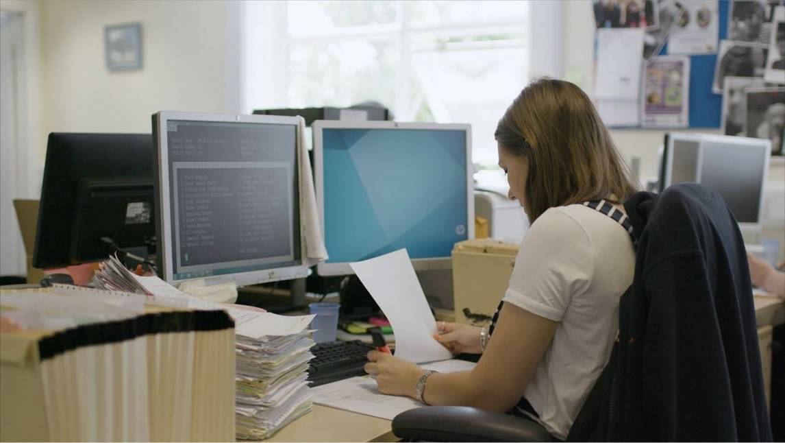 Woman in office processes Accounts Payable paper invoices in front of computer