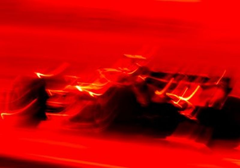 A Formula One race car captured at low shutterspeed and in full red colour tone, producing blurred lines that give an artistic look to match the speed of the car.