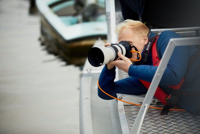 Photographer Matthew Joseph lies on his side at the water's edge, shooting with a Canon EOS R camera and Canon RF 70-200mm F2.8 L IS USM lens.