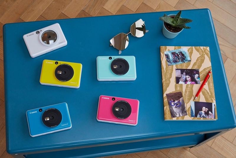 Canon Zoemini C and Canon Zoemini S on a table with a notebook with pictures stuck to it.