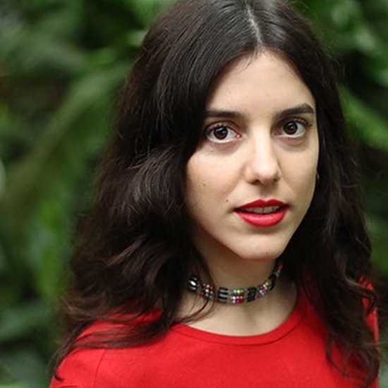 Portrait of a woman with dark hair and a red top, against blurred green plants.