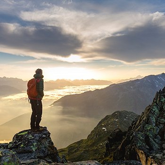 A hiker stands on top of a tall mountain at dawn.