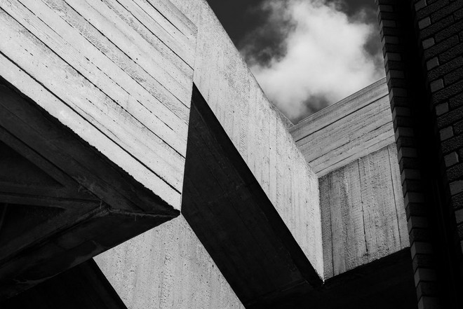 صورة بالأبيض والأسود لمبنى من الخرسانة تم تصويره من الأسفل لإنشاء أشكال هندسية مزودة بظلال.