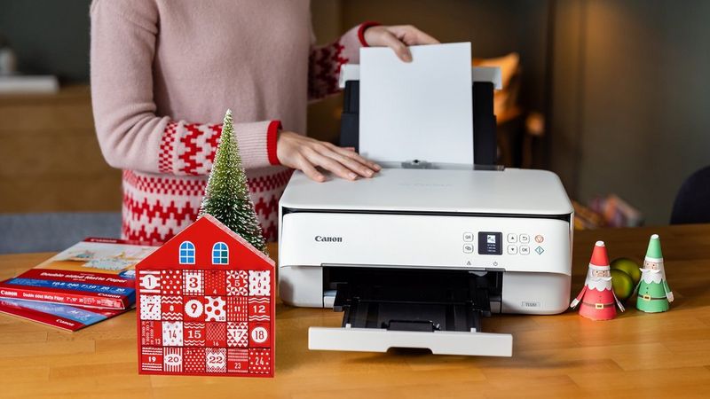 A handcrafted paper Advent calendar sits on a wooden table next to a Canon PIXMA printer, with some Canon paper and other Christmas themed papercraft behind.