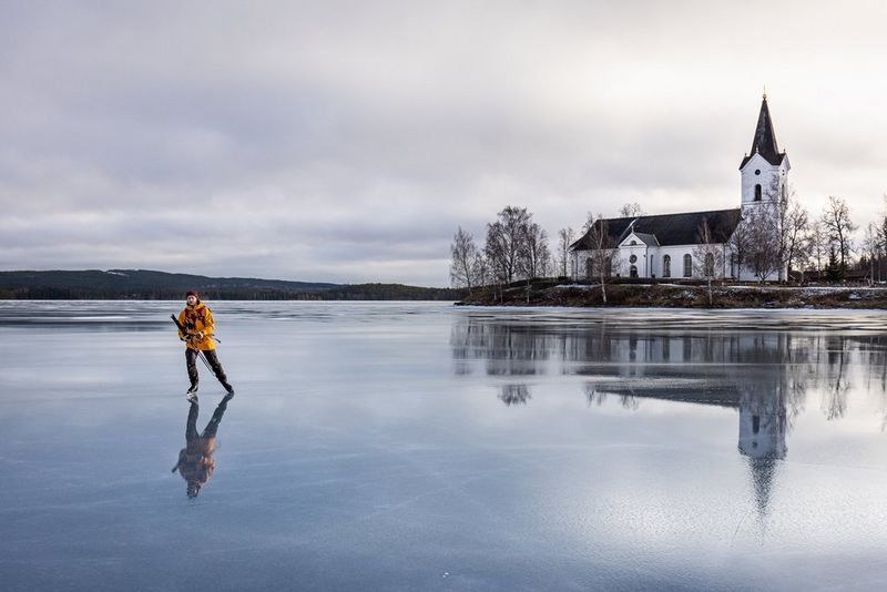 Kollases jakis mees uisutamas mööda külmunud järve. Jääl paistab taustal oleva valge kiriku peegeldus.