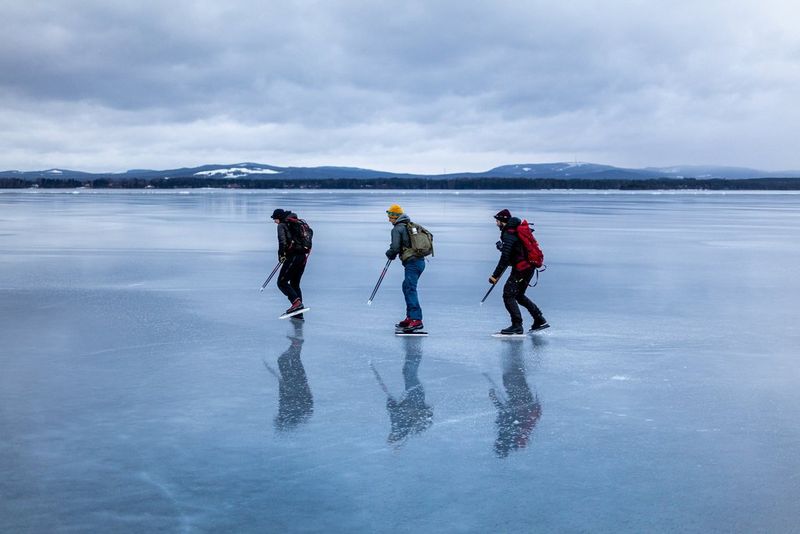 ثلاثة متزلجين يحملون حقائب ظهر يجتازون بحيرة مجمدة شاسعة. يمكن رؤية القمم المغطاة بالثلوج من مسافة بعيدة.