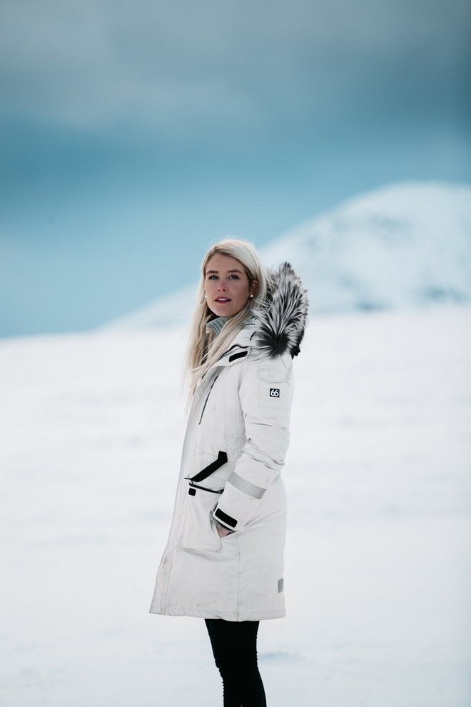 تقف مصورة المناظر الطبيعية أوشا شتاينر وتضع يديها في جيوبها في مكان ثلجي وهي ترتدي معطفًا شتويًا طويلاً أبيض اللون.