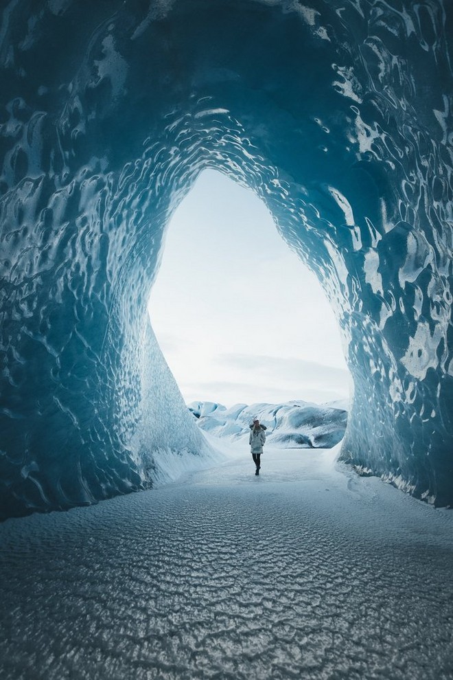 مصورة المناظر الطبيعية أوشا شتاينر تمشي داخل كهف جليدي أيسلندي ضخم وهي ترتدي ملابس شتوية دافئة.
