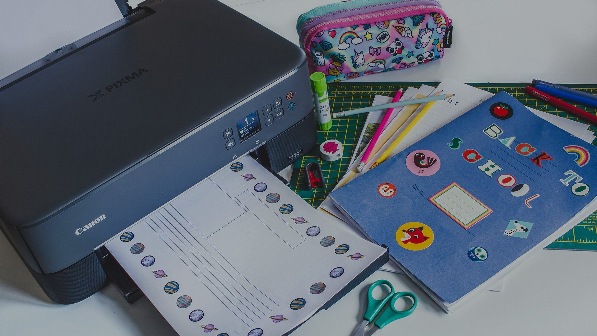 A Canon PIXMA TS5340 printer next to school books, a pencil case and a pair of scissors.
