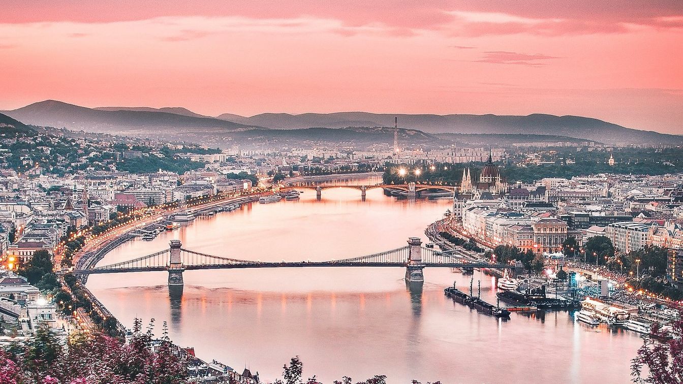 مشهد فوق نهر الدانوب على تل غيليرت بمدينة بودابست في المجر من موقع مرتفع تكسوه درجات من اللون الأحمر البرتقالي.