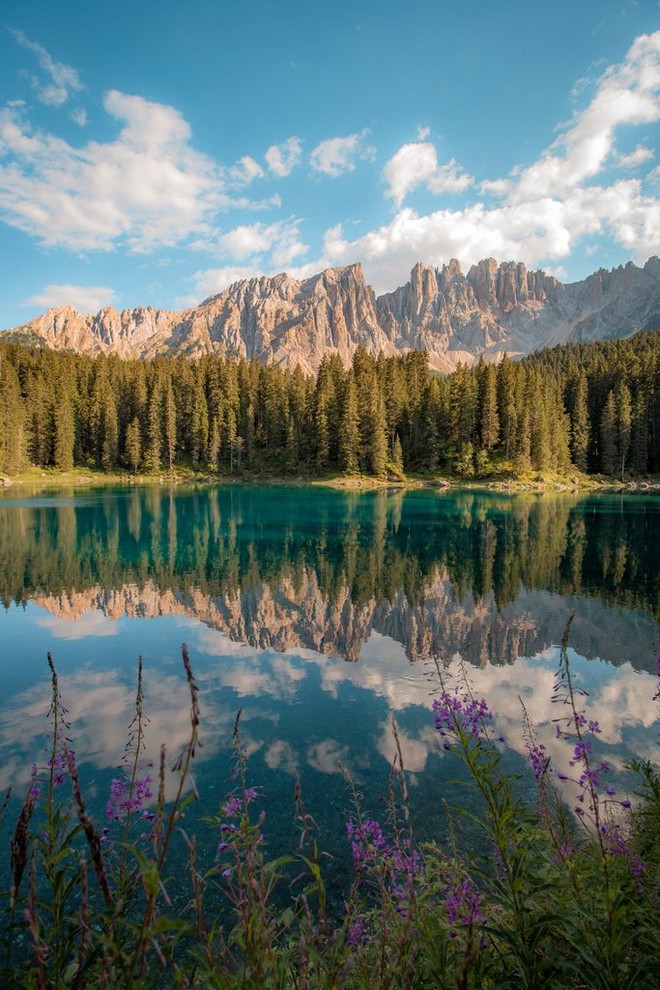 بحيرة كاريزا في مقاطعة جنوب تيرول بإيطاليا في يوم صيفي مشرق وتنعكس جبال دولوميت في الخلفية على مياه البحيرة الساكنة.