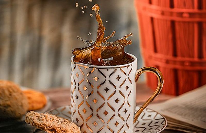 Tea splashing up into the air from a tall patterned mug on a saucer.