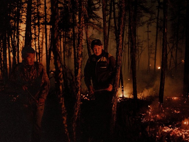 رجلان يمشيان في غابة مظلمة يأتي مصدر الضوء الوحيد فيها من التوهج المشتعل حولهما.