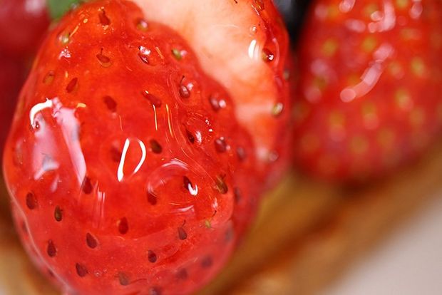 A fruit flan filled with strawberries and garnished with a basil leaf.