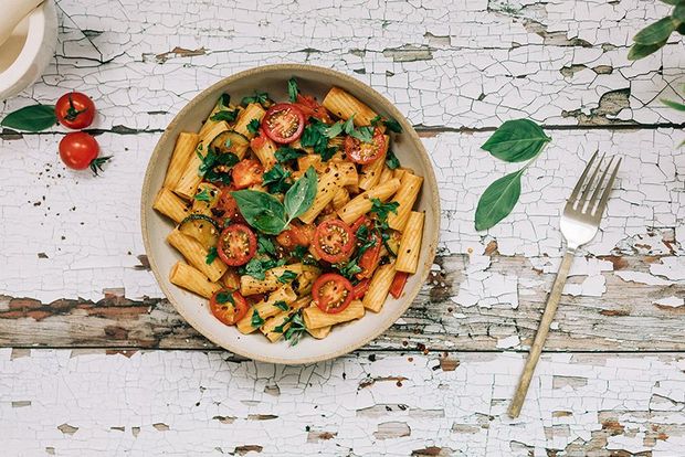 A bowl of tomato and basil pasta, shot top down with a fork, basil leaves and pestle and mortar in frame.