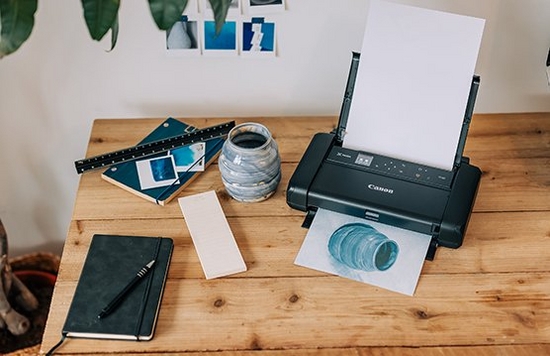 A Canon PIXMA TR150 prints out a picture of a small blue vase, the inspiration for which is positioned next to it.