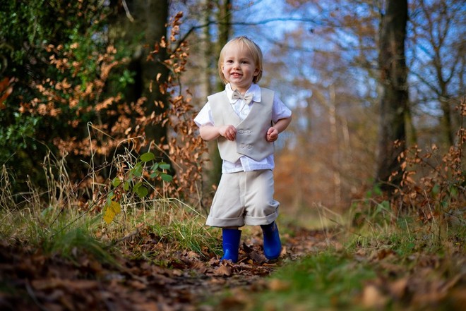 ولد صغير يرتدي صدرية بيج وحذاء أزرق فاتحًا ويركض عبر فسحة في الغابة.