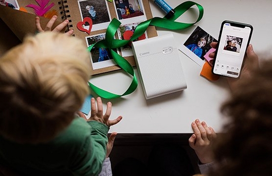 A Canon SELPHY SQUARE QX10 printer next to a scrapbook filled with small prints.
