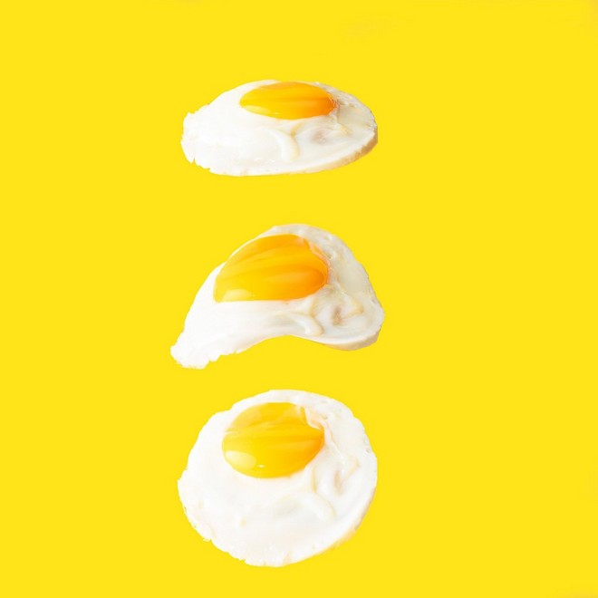 ثلاث بيضات مقلية تبدو عائمة ومرتبة في خط واحد على خلفية باللون الأصفر.