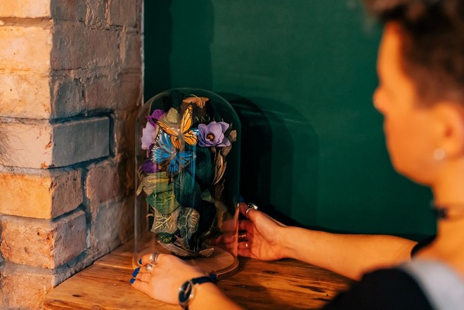 امرأة تضع قبة زجاجية مليئة بفراشات ورقية ملونة على سطح خشبي.