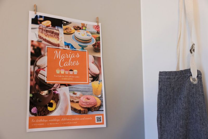 Плакат организации Maria's Cakes закреплен на стене; по центру плаката можно увидеть логотип компании в окружении тортов.