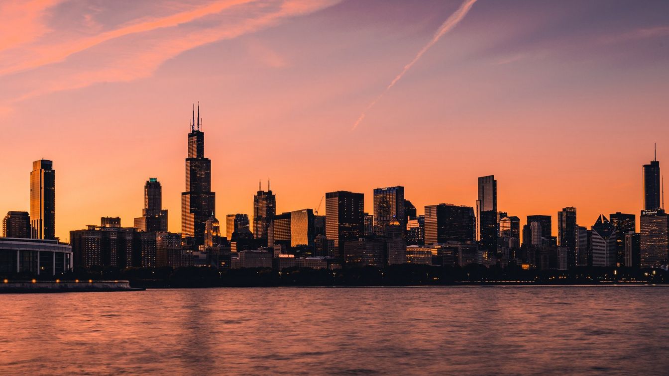 أفق مدينة شيكاغو في أثناء الساعة الذهبية مع وجود ماء أمام المباني. يمتزج المشهد بالكامل بتوهج الأفق بالون البرتقالي.