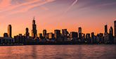 The Chicago skyline during golden hour, with water in front of the buildings. The entire scene is tinged with the orange glow of the horizon.