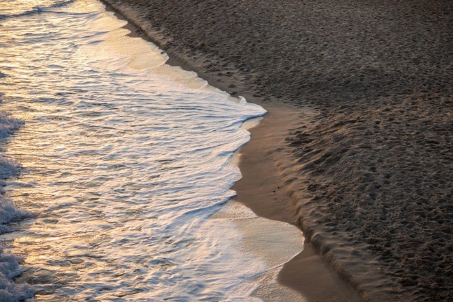 تتلاطم رغوة ماء البحر على شاطئ رملي عند الغسق.