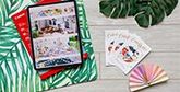 A tablet displaying the Creative Park app sits on botanical themed paper, next to custom invitations and colourful bunting. 