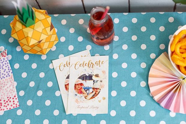 Personalised cards created with the Creative Park app on a party table with paper garlands and a pineapple gift box.