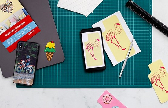 A green cutting mat with printed stickers resting on top, with a smartphone and tablet. 