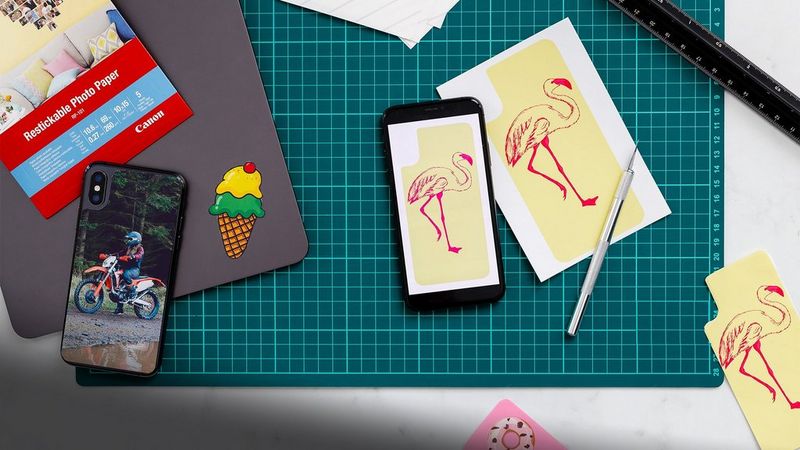 A green cutting mat with printed stickers resting on top, with a smartphone and tablet.