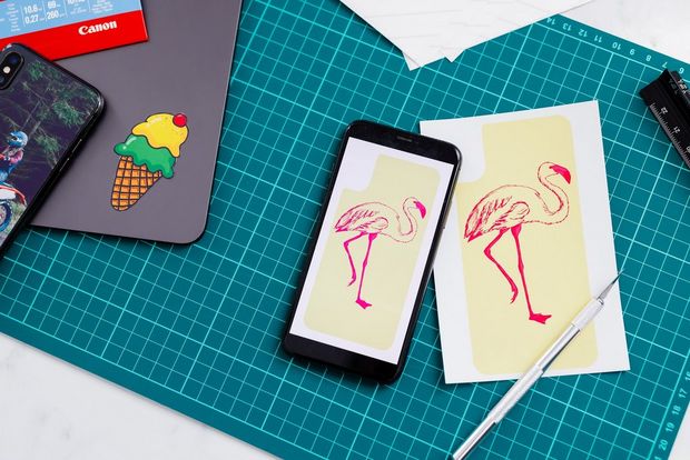 A smartphone showing Creative Park, a tablet with printed stickers on it and a green cutting mat. 