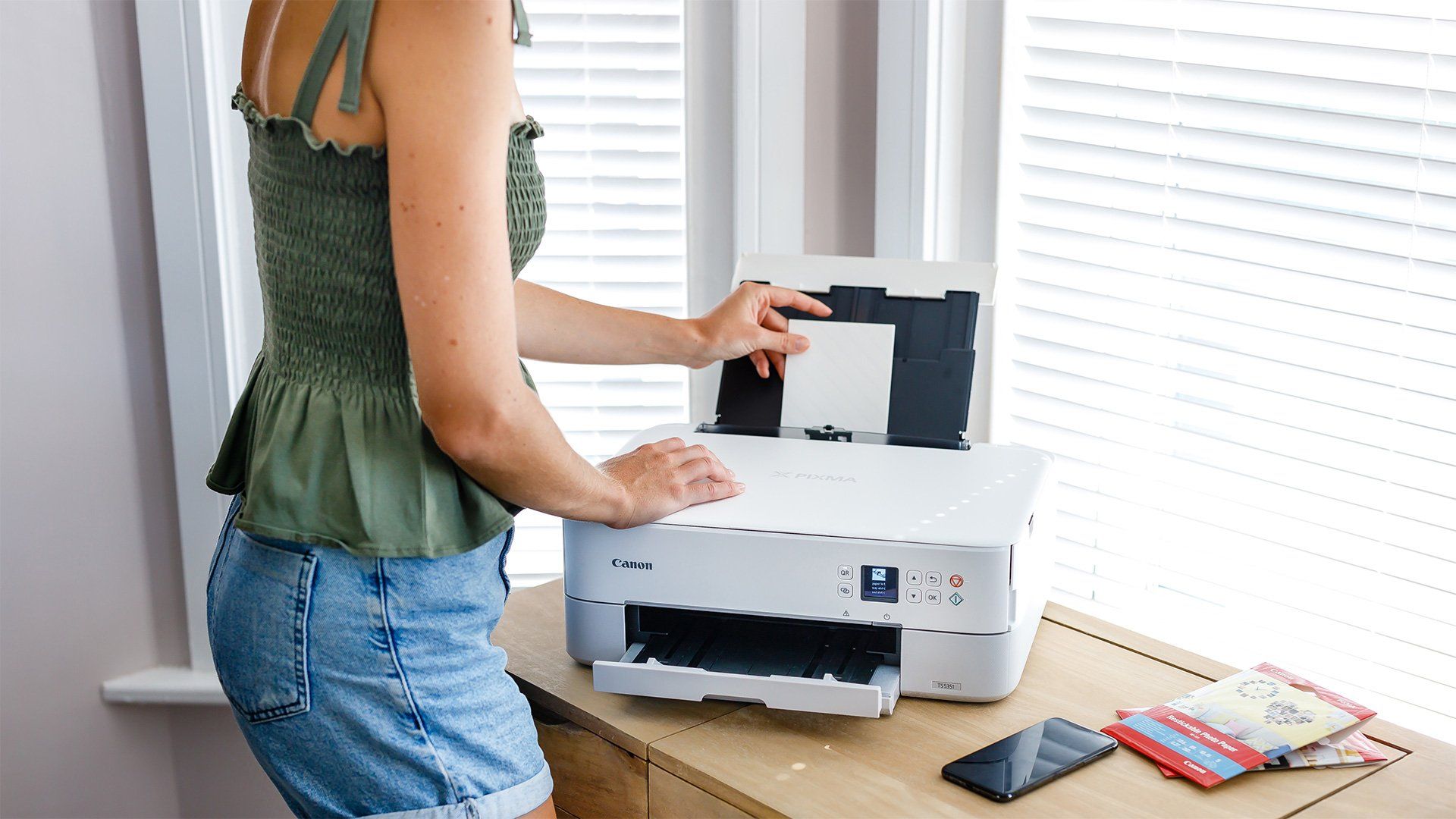 A woman loading photo paper into a white Canon PIXMA printer. 