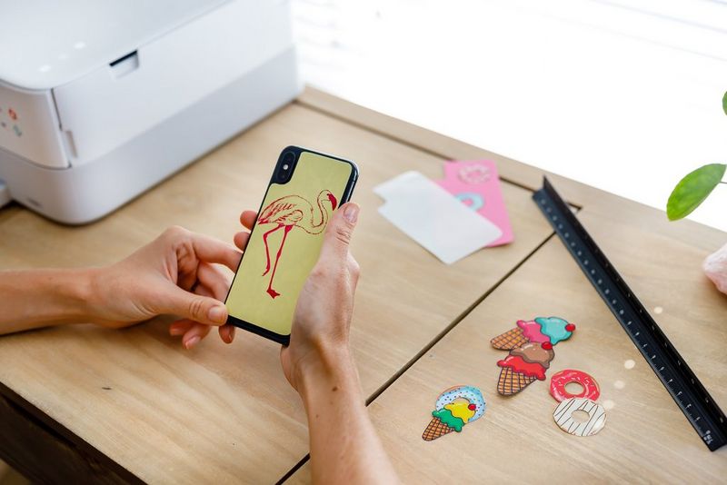 A woman applying a cut-out printed sticker to the back of her smartphone. 
