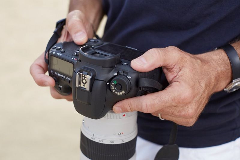 A man's hands hold a Canon camera facing down.