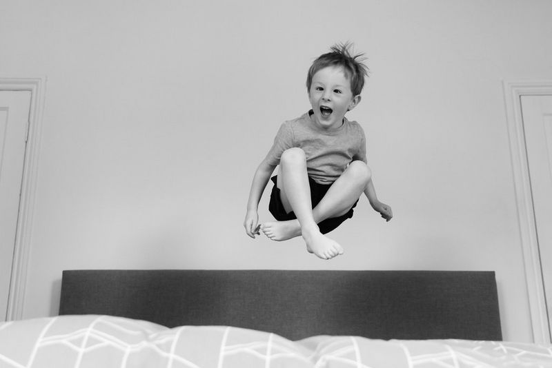 صورة بالأبيض والأسود لصبي صغير يضحك بينما يقفز على سرير.