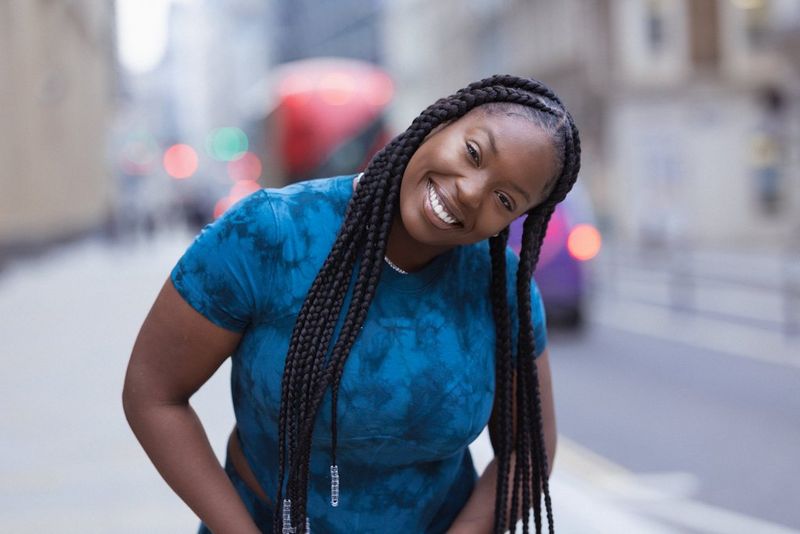 A portrait of a smiling woman with long braids wearing a blue tie dye t-shirt.