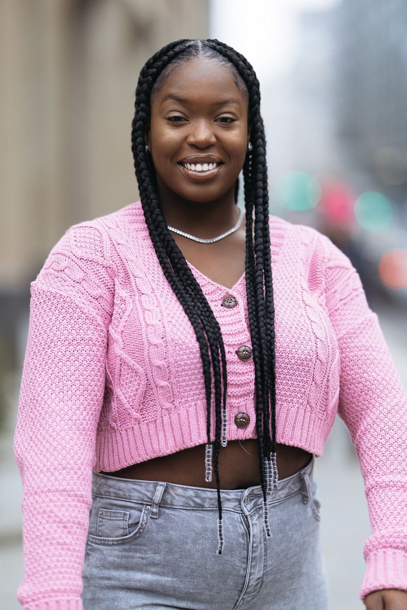 A woman with long braids wearing a pink cardigan.