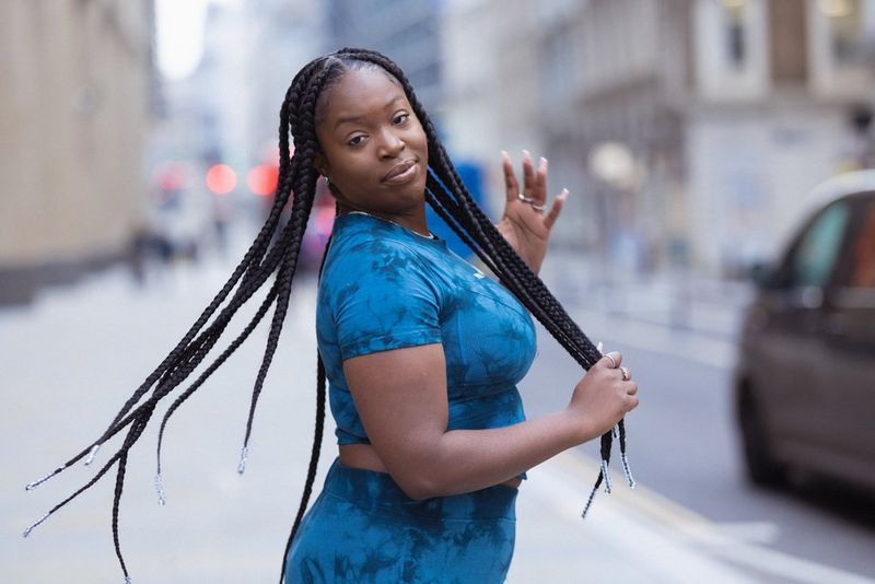 A woman wearing a blue tie-dye outfit flicks her long braids behind her.