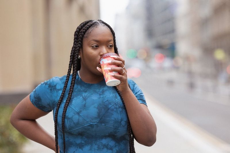 A woman in a tie-dye t-shirt drinks from a takeaway cup.