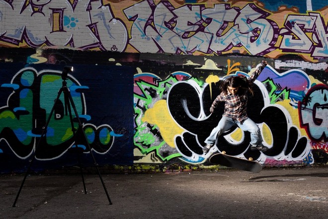 Скейтбордист выполняет трюк перед стеной с граффити; фотография создана с помощью вспышки Speedlite, установленной на штатив.