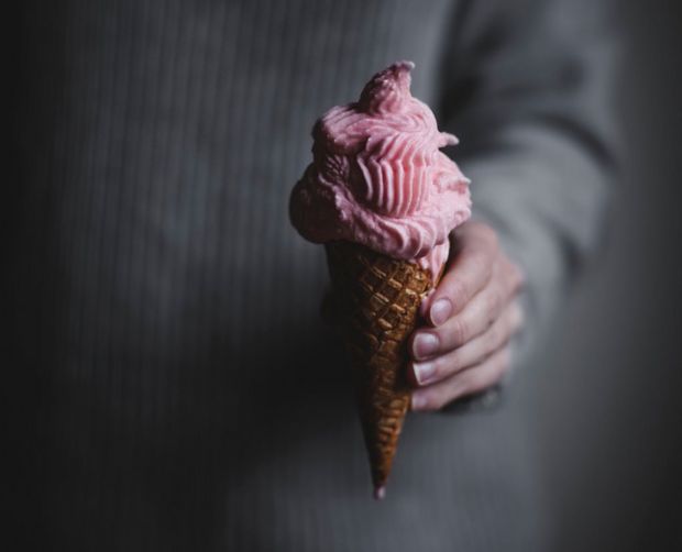 A person in a grey jumper golding a pink ice cream in a waffle cone. 