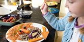 A young girl creating a face out of food on a plate.