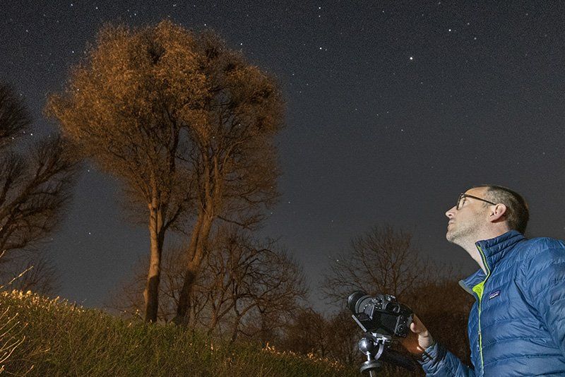 A photographer sets up a tripod in his garden to take a photo of the night sky.