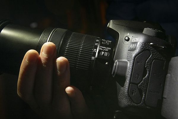 A photographer’s hands holding a Canon EOS 90D with a zoom lens attached.