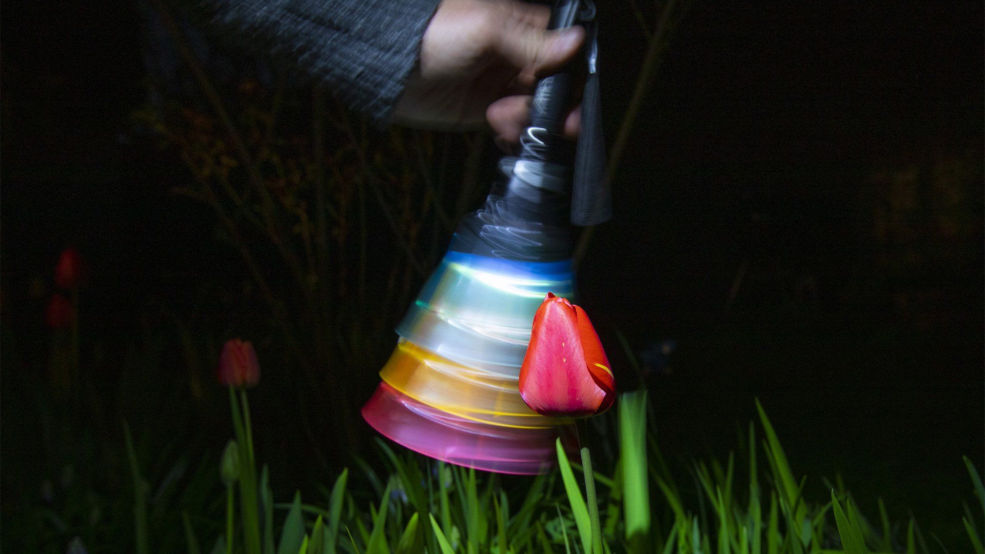 A hand waves a torch with colourful cups taped to the end, causing it to blur.
