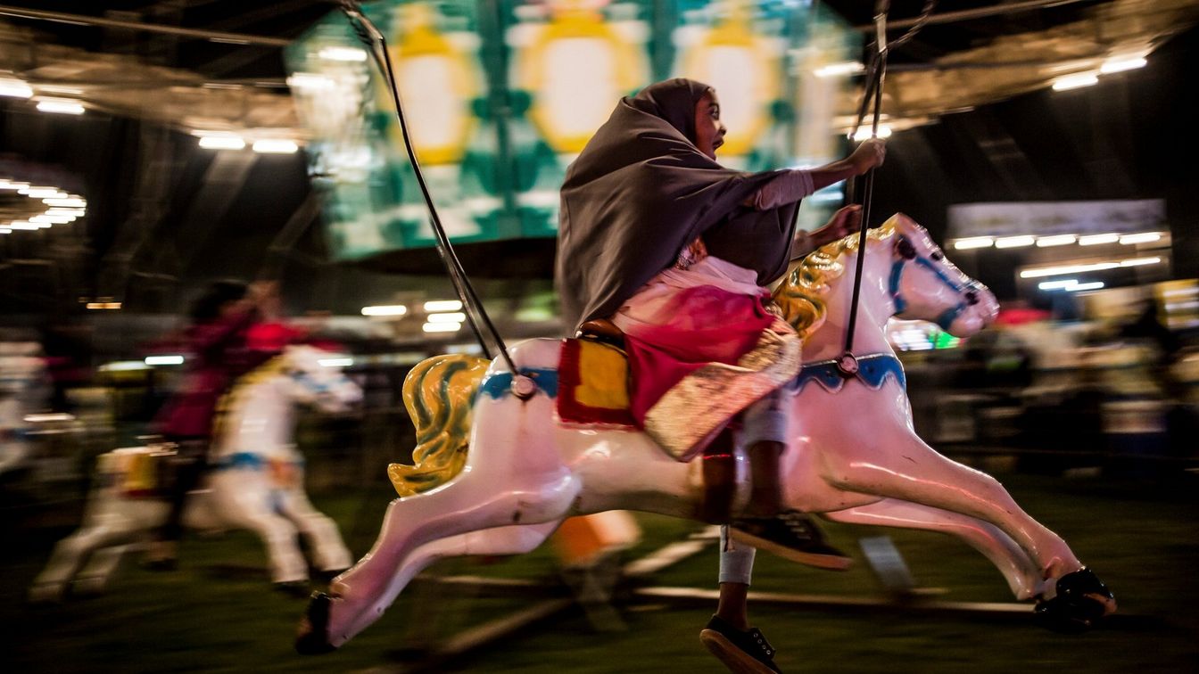 فتاة مسلمة صغيرة تصرخ بفرح وهي تركب على حصان في أرجوحة دوارة في جوهانسبورغ بجنوب إفريقيا.